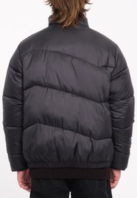 Zwarte pufferjack met diagonaal doorgestikt patroon, hoge kraag, elastische zoom en glanzende textuur. Heeft een verlaagde schouderlijn en een ontspannen fit.