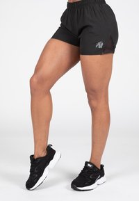 Zwarte sportshorts met een elastische tailleband, netten zijpanelen en een klein logo; gecombineerd met zwart-witte hardloopschoenen.