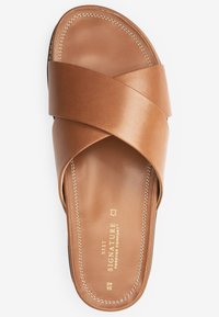 Bruine leren slipper sandalen met een kruislingse bandontwerp, een zachte textuur en contrasterende witte stiksels. Heeft een merketiket op de binnenzool.