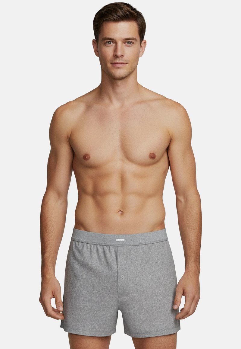 Boxer grigi in cotone con elastico in vita, dotati di chiusura frontale con bottoni e una texture liscia. Modello in piedi con torso nudo.