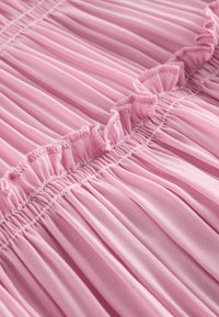 Close-up af pink plisseret stof med en rynket søm og små flæsedetaljer langs syningslinjen.
