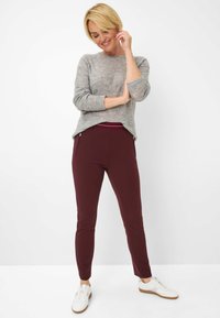 Grauer Strickpullover mit gerippten Bündchen und Saum, kombiniert mit burgunderrot taperd Hosen mit schmalem Schnitt und Reißverschlusstaschen, getragen mit weißen Sneakers.