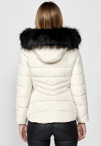 Giubbotto puffer in avorio con colletto in pelliccia sintetica nera, caratterizzato da un design a zig-zag e tasche laterali.