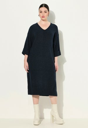 Robe en tricot bleu marine avec un décolleté en V, des manches trois-quarts et des détails de poignets côtelés. Silhouette mi-longue, texture douce et design simple.