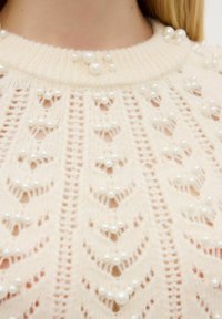 Maglione lavorato a maglia in morbido crema con un motivo testurizzato caratterizzato da decorazioni in perle. Collo a girocollo a coste e delicate finiture a punto sparso in tutto il capo.