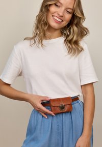 Bijela majica kratkih rukava u kombinaciji s traper suknjom. Skupljač od smešane kože smeđeg tonusa s metalnom kopčom naglašava odjevnu kombinaciju.