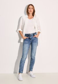 Camisa de lino blanca ligera sobre una camiseta blanca ajustada, combinada con vaqueros ajustados de color azul claro y zapatillas blancas. Un atuendo simple y casual.