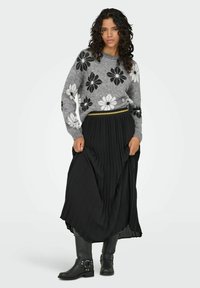 Hallukatehall vest, millel on mustad ja valged lillemustrid, koos musta plisseeritud seelikuga. Mustad pahkluu saapad, millel on pandla detail, täiendavad komplekti.