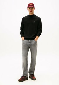 Suéter negro de cuello alto, jeans de denim gris y zapatillas multicolores. Los accesorios incluyen una gorra burdeos con el logotipo de "Tommy".