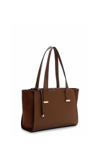 Borsa tote in pelle marrone con due manici lunghi, zip dorata e piccolo logo dorato del marchio sul davanti, vista angolata su sfondo bianco.