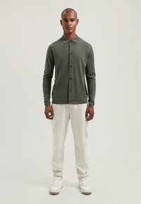 Donkergrijze lange mouwen cardigan met een kraaghalslijn, knopen aan de voorkant, gecombineerd met lichtgekleurde broeken en witte sneakers. Gladde textuur.