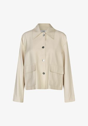 Chaqueta beige hecha de tela suave, con cuello puntiagudo, botones plateados y dos grandes bolsillos frontales. Mangas largas y diseño de corte relajado.