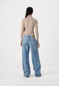 Jersey beige de cuello alto combinado con unos vaqueros de pierna ancha azules. Los vaqueros cuentan con un parche en la parte posterior y un diseño clásico de cinco bolsillos.