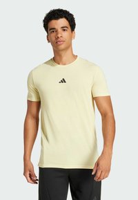 Camiseta deportiva de manga corta en amarillo claro, hecha de un tejido suave, con un pequeño logo triangular negro en el pecho.