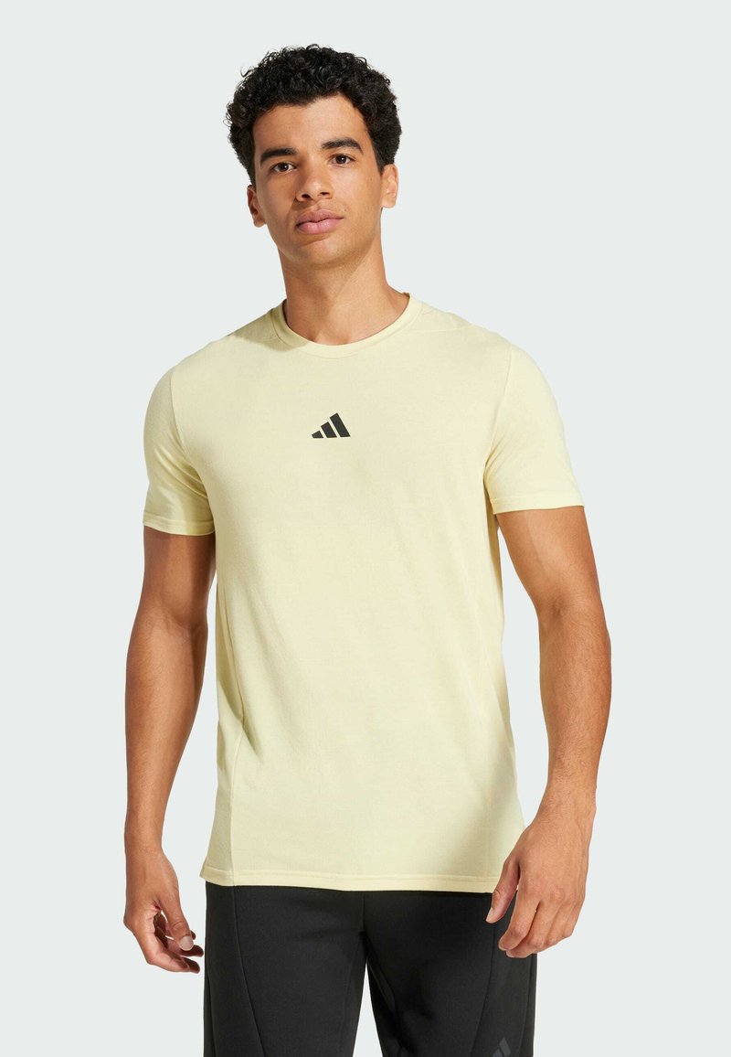 Camiseta deportiva de manga corta en amarillo claro, hecha de un tejido suave, con un pequeño logo triangular negro en el pecho.
