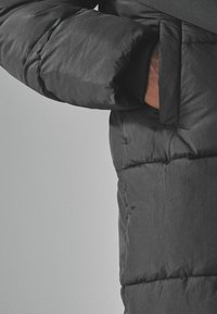 Pufferjakke i mørkegrå, med en quiltet design, en blød tekstur og en sidelomme med en åben flapdetalje.