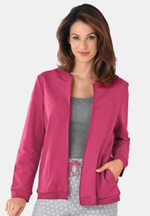 Fuchsia ritjasje met zijzakken en omgeslagen mouwen, gedragen over een grijze top, aangevuld met grijze onderkant met sterrenpatroon.