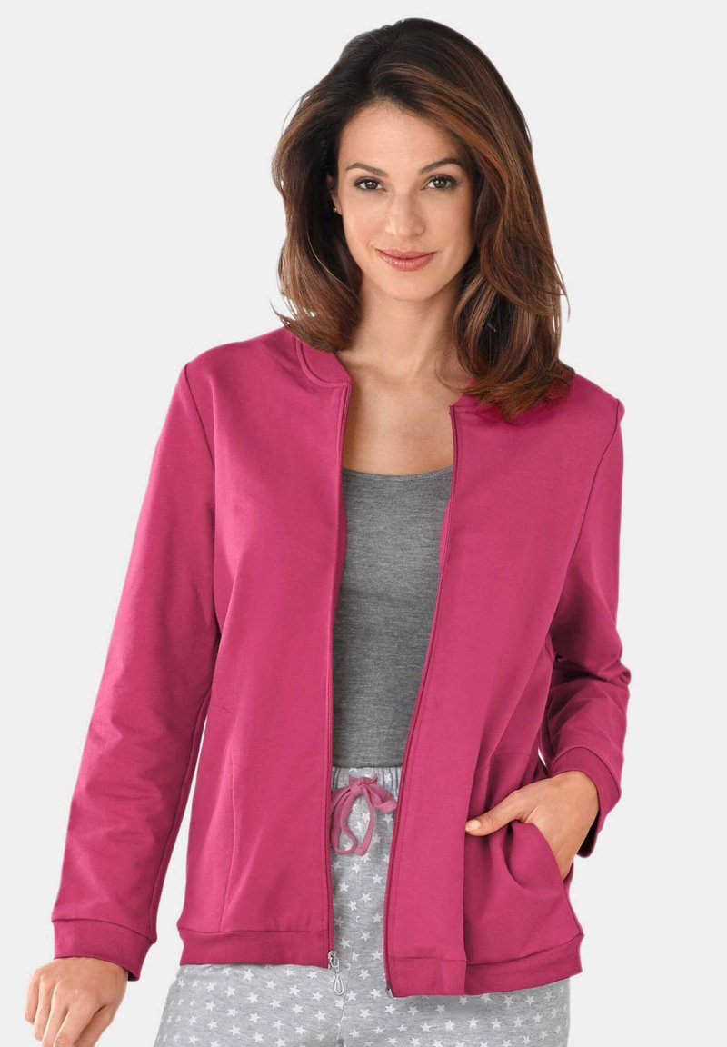 Veste fuchsia zippée avec poches latérales et manches à revers, portée par-dessus un haut gris, complétée par un bas gris à motifs d'étoiles.