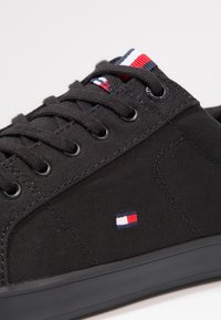 Schwarze Leinensneaker mit schwarzen Schnürsenkeln, Ösen und einer Gummisohle. Verfügt über ein kleines, mehrfarbiges Logo-Patch an der Seite.