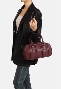 Borsa in pelle borgogna con una texture liscia, caratterizzata da due manici superiori, una chiusura con zip e dettagli a pannello verticali.
