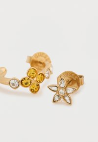 Σκουλαρίκια σε χρυσό τόνο με σχέδια λουλουδιών. Το ένα διαθέτει κίτρινες και διαφανείς στρας, ενώ το άλλο είναι διακοσμημένο με διαυγή λίθους κομμένους σε σχήμα μαρκίζ.