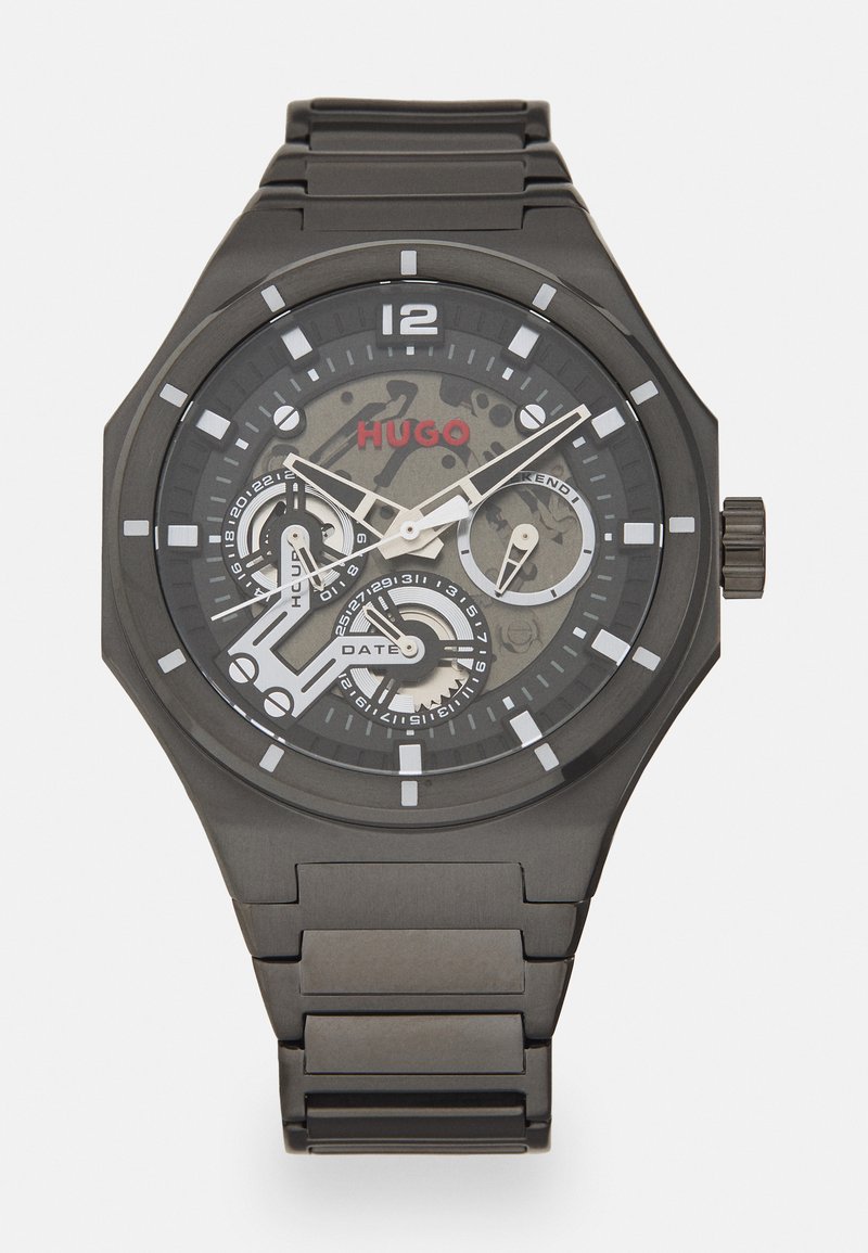 Black stainless steel watch with a round face, white hour markers, and a camouflage pattern. Features date and chronograph sub-dials. Red "HUGO" logo.