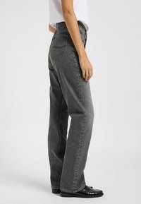 Vaqueros de denim gris con un corte relajado, que cuentan con cinco bolsillos, costuras visibles y una textura ligeramente deslavada. Llevados con mocasines negros.
