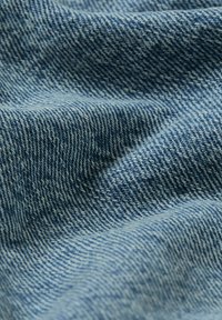 Ljusblå denimtyg med en strukturad yta. Har ett klassiskt twill-vävmönster med synliga sömmar och lätta rynkor.