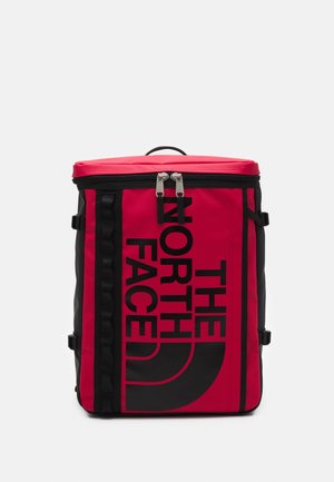 Czerwony prostokątny plecak z czarnym pionowym zamkiem błyskawicznym, czarnymi uchwytami i dużym czarnym logo "The North Face" na przednim panelu.