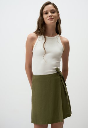 Débardeur blanc à côtes associé à une jupe enroulée vert olive arrivant au genou, ornée d'une ceinture à nouer à la taille. Tissu doux et léger.