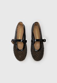 Chaussures Mary Jane noires avec texture décorative perle, une bride en cuir verni, et un design à bout arrondi avec une semelle intérieure beige.
