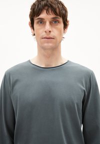 Langärmliges graues Shirt aus weichem Stoff, mit Rundhalsausschnitt und minimalen Nähdetails. Glatte Textur mit lockerem Schnitt.