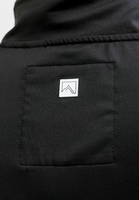 Mustast sweatshirt kangast, millel on ruudukujuline tasku ja väike valge logo. Sile tekstuur, õmmeldud servad, minimalistik disain.