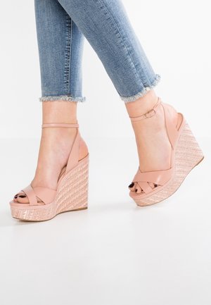 Nærbillede af fødder iført lyserøde kilehælssandaler med ankelsnore og tekstureret platform, kombineret med blå jeans med frynset kant.