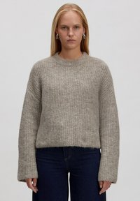 Lichtgrijze gebreide trui met een ribbelstructuur, ronde hals en lange mouwen, in combinatie met donkerdenim jeans.