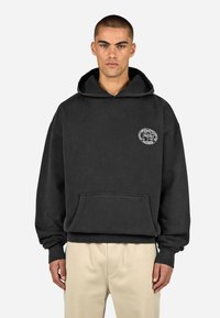 Čierna mikina s kapucňou vyrobená z mäkkej tkaniny, obsahuje klokaní vrecko a ryhované manžety. Zaujímavým detailom je malá okrúhla grafika na hrudi.