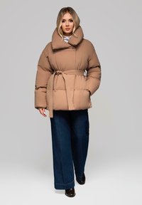 Brun polstret jakke med en bred foldet krave, belted talje og lange ærmer; parret med mørkeblå brede bukser og sorte sko.