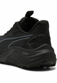 Baskets noires de sport présentant une tige en maille texturée, des lignes épurées et une semelle rembourrée avec un design en forme de vague ; logo sur le côté.