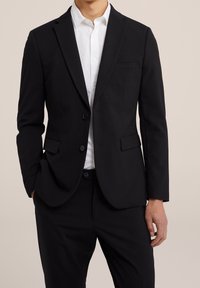 Svart kavaj med skräddarsydd passform, enstaka knappstängning, snibbkragar och en bröstficka, tillsammans med en vit skjorta med krage.