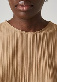Beige plisséd topp med rund halslinning, teksturert stoff og en jevn finish i kanten. Uthevet med subtile sømdetaljer.