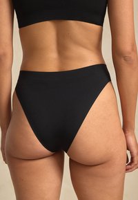 Svart högmidjad bikinibyxa med slät matt textur, minimal täckning och rena linjer. Har en sömlös design för komfort.