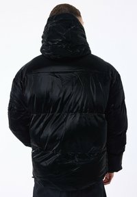 Sort pufferjakke med hætte, der har en blank, quiltet tekstur og vandret syninger. Vist fra ryggen uden synlige logoer.