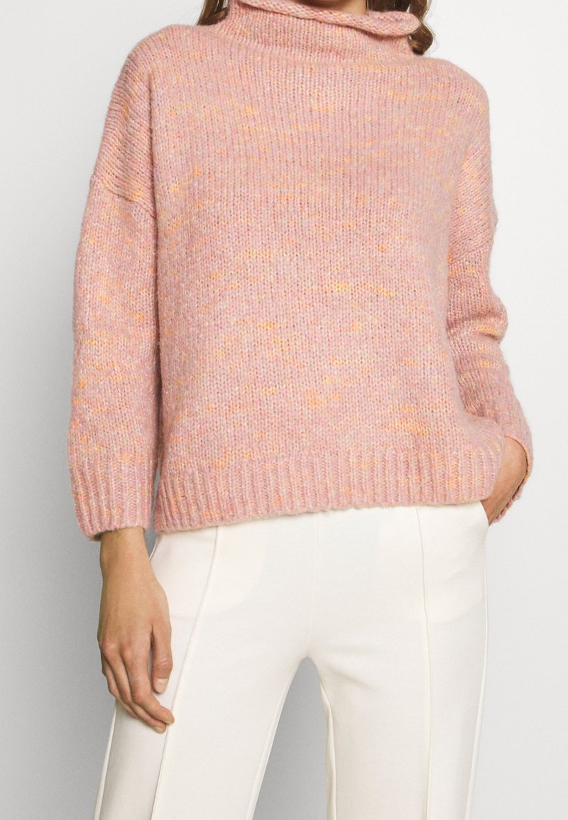 Chunky rosa tröja med en hög, vikbar krage, korta ärmar och ett ribbat avslut, som har inslag av orange fläckar genom hela stickningen.