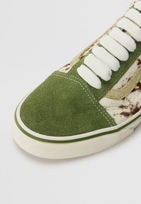 Botte en daim vert à l'avant avec des lacets blancs, côtés en tissu imprimé animal brun et blanc, et semelle en caoutchouc écru avec une bande verte.