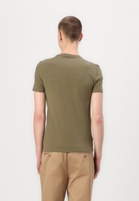 Oliven grøn kortærmet t-shirt, tætsiddende design, blød tekstur, rund halsudskæring, glat stof. Båret med beige bukser, vist fra bagvyn.