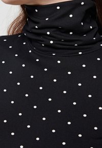 Svart polotröja med en figurnära design och vita prickar. Tillverkad i ett mjukt tyg med en slät yta.