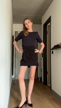 Top negru cu maneci lungi si fusta neagra mulata cu un design in culise. Modelul sta in tocuri negre ascutite pe un podea de lemn.