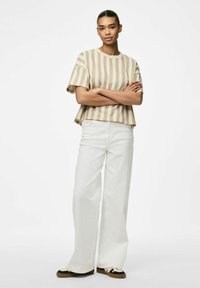 Top a maniche corte beige e bianco a righe, con una vestibilità comoda, abbinato a pantaloni bianchi a vita alta e gamba larga e scarpe da ginnastica con accenti neri.