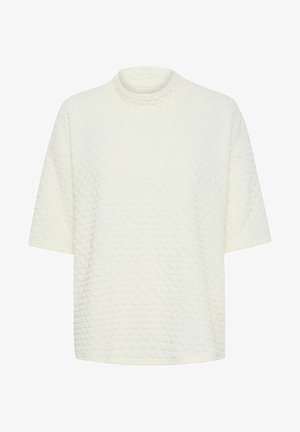 Površinski strukturirani gornji dio boje krem s lažnim ovratnikom, kratkim rukavima i opuštenim krojem. Sadrži uzorak podignutih dijamanata kroz cijeli gornji dio.