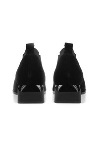 Pari mustia mokkanahkaisia nilkkureita, joissa on paksut korot, nähtynä takaa valkoisella taustalla.